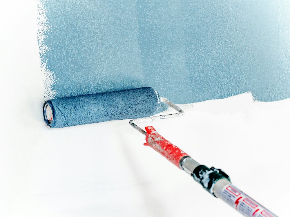 Paint roller applying blue paint to a white wall